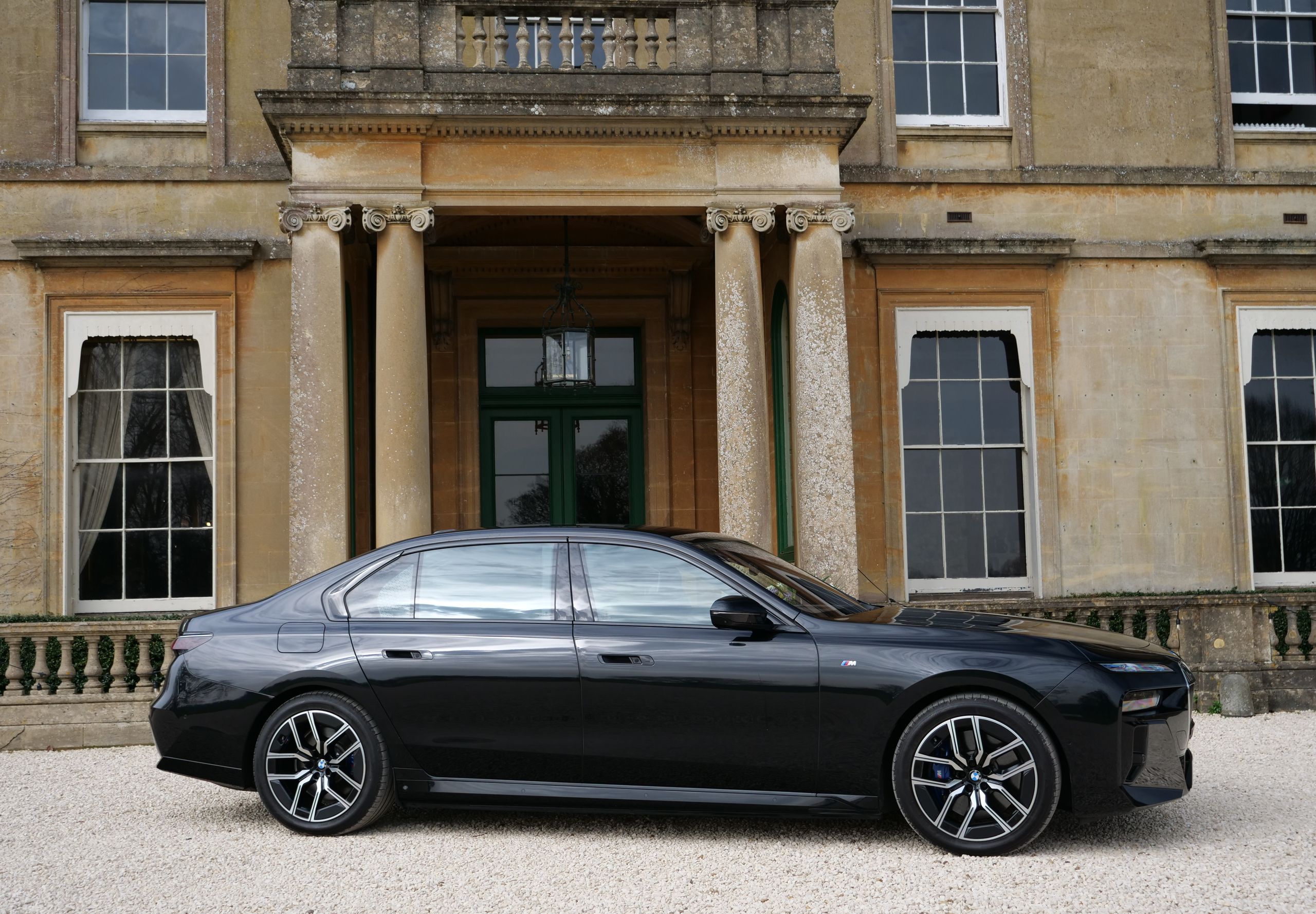 A black chauffeur saloon parked side-on in front of the columned portico of a Georgian Bath-stone house