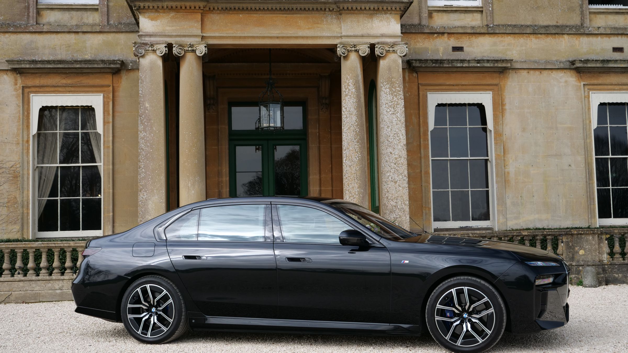 A black chauffeur saloon parked side-on in front of the columned portico of a Georgian Bath-stone house