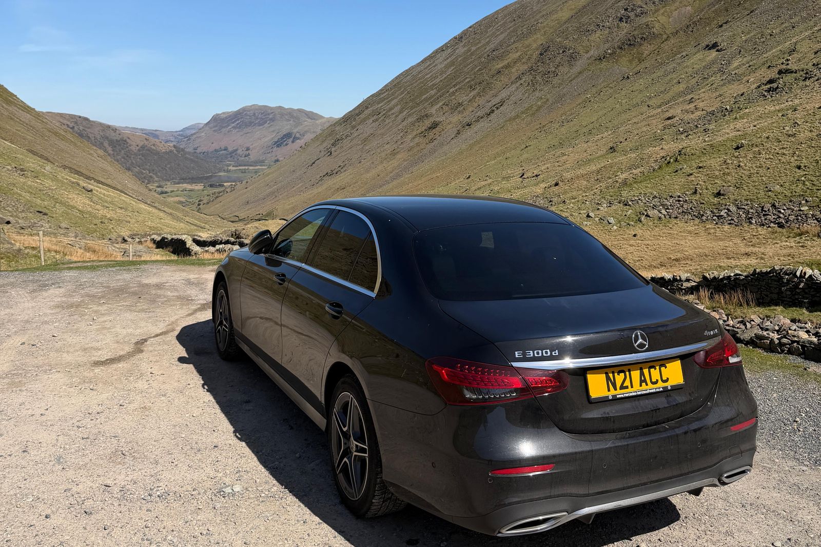 A black Mercedes saloon parked above a long green valley in the Lake District