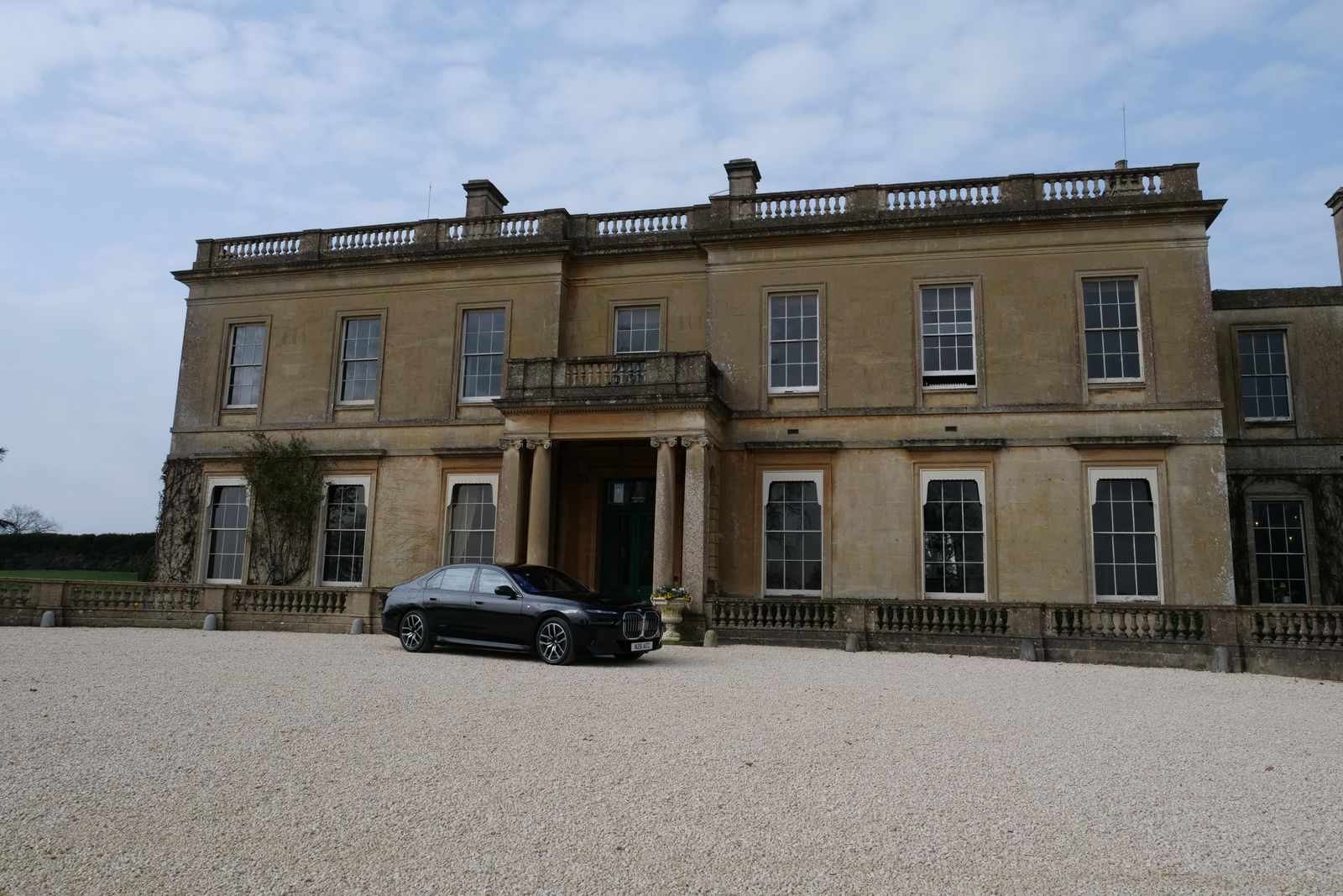 A chauffeur car waiting on the gravel in front of a Georgian country house